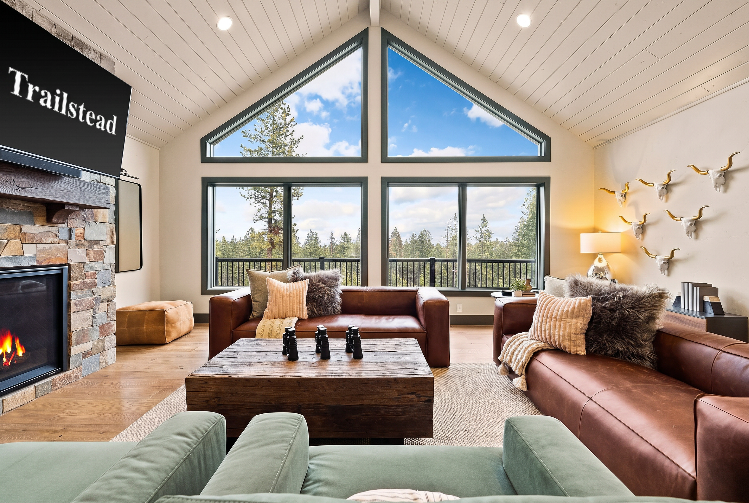 The Tamarack — living room with vaulted ceiling, large windows, brown leather sofas, coffee table, and stone fireplace
