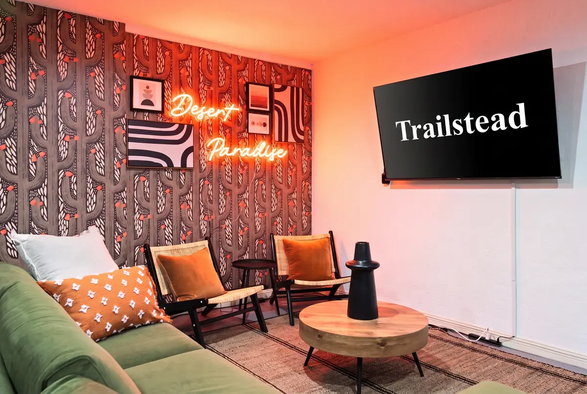 The Sunkiss — seating area featuring a green sofa, accent chairs, neon wall sign, and a wall-mounted television
